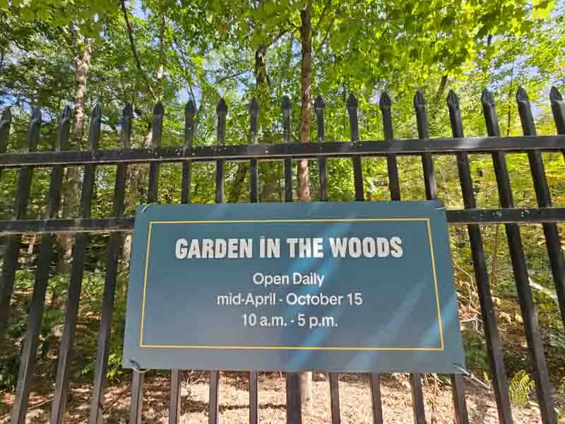 Sign on a fence: Garden in the Woods, Open Daily, mid-April - October 15, 10 a.m. - 5 p.m.